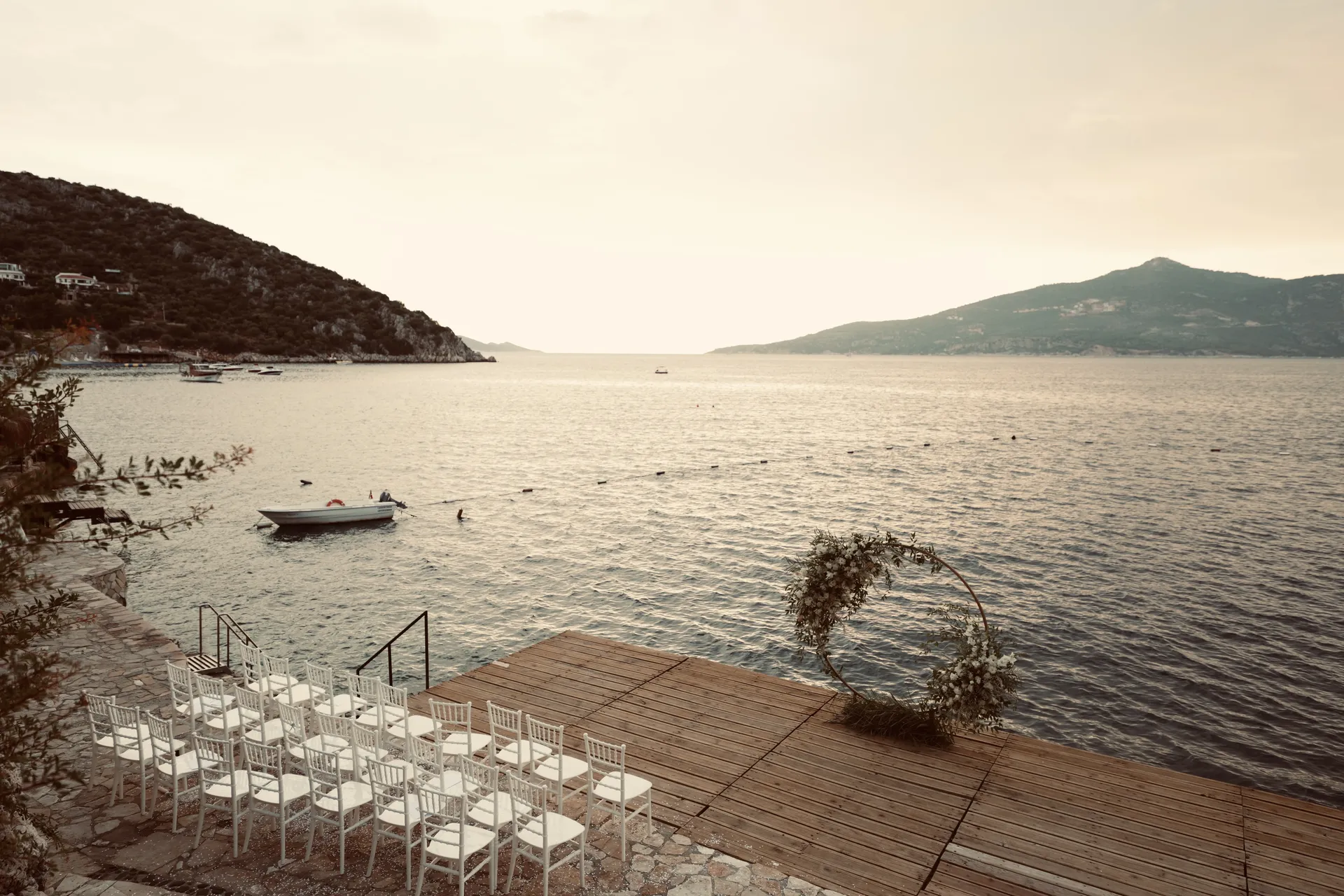 Empty ceremony setup with white chairs on wooden deck overlooking sea